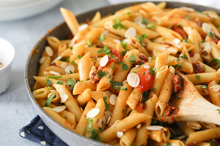 Vegan Sun Dried Tomato Pasta in gray pan with wooden spoon