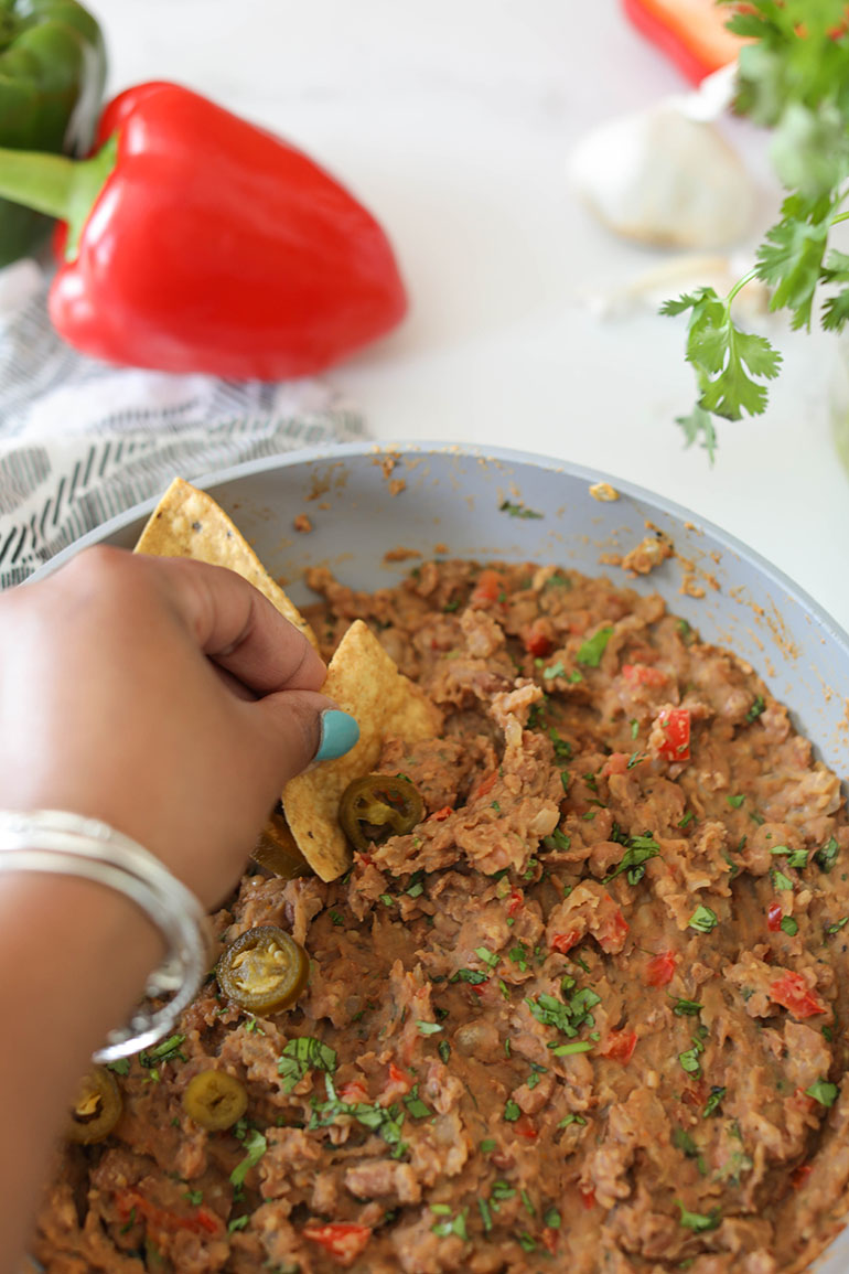 Brown hand scooping vegan Refried Beans in pan